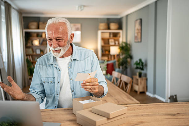 istock Senior man opening package and reading greeting card during video call 2202830316