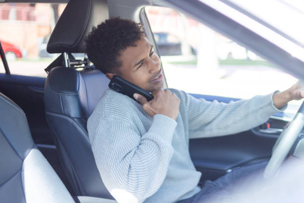 istock Young man driving dangerously while holding a phone between his shoulder and ear 2202830400