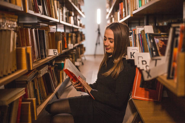 istock Woman reading a book while sitting between bookshelves 2202830401