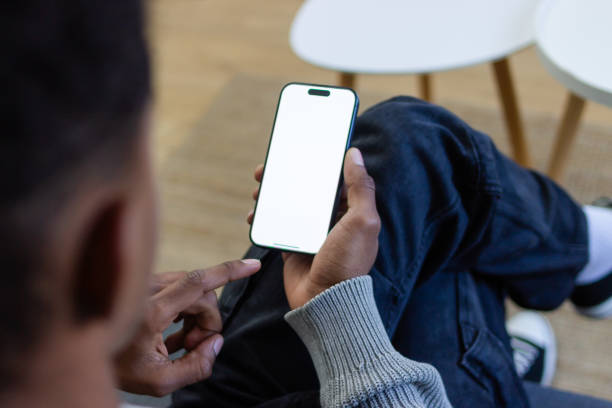 Young man relaxing on sofa using smartphone with blank screen Young man is relaxing on sofa and using smartphone with blank white screen man looking at phone over shoulder stock pictures, royalty-free photos & images