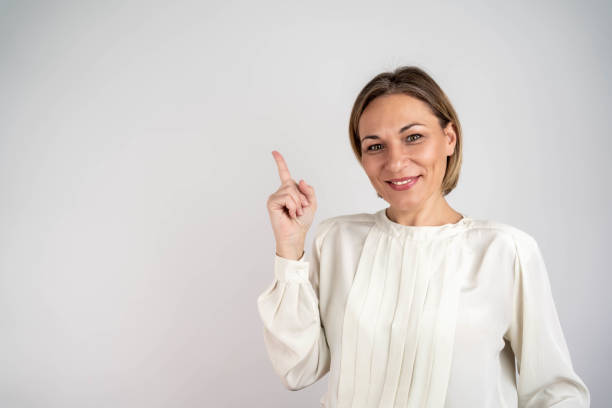 Happy smiling caucasian mature woman with toothy white smile looking at camera pointing showing copy space free space isolated in white background. beautiful woman pointing at copyspace looks in camer