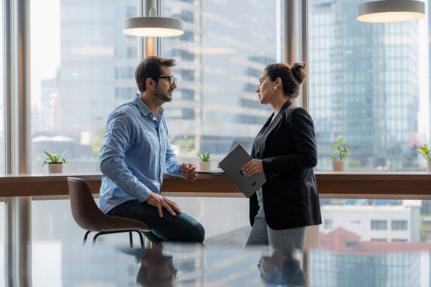 istock Two business professionals collaborating at a modern office desk by a window overlooking a bustling city skyline. Business strategy, teamwork, data analysis, and innovation using a digital tablet for corporate planning and decision-making. 2202836248