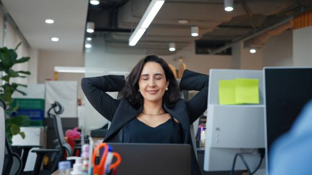 Entrepreneur stretching arms and leaning back in office chair for relaxation while working on laptop in a coworking space. Exhausted businessman taking a break to relieve stress. Healthy workplace lifestyle, flexibility, and corporate wellbeing.