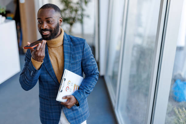 Businessman talking on speakerphone while holding clipboard with charts in modern office