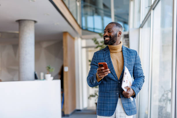 istock Smiling businessman walking in modern office holding smartphone and documents 2202844829