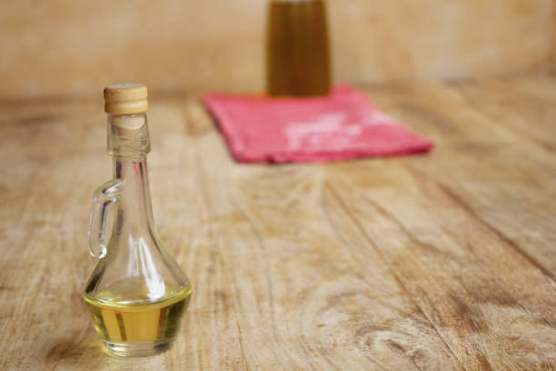 Bottle and bowl with rosemary-essential oil on wooden bench with food and rosemary sprigs and kitchen in background. Front view.