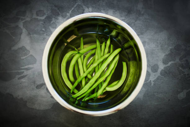 Close-up of vibrant green beans submerged in water inside a shiny stainless steel bowl, creating a fresh and clean food preparation scene.