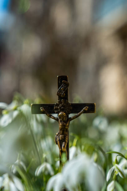 A metal crucifix depicting Jesus on the cross stands among delicate white snowdrop flowers, symbolizing faith, sacrifice, and renewal in nature.
