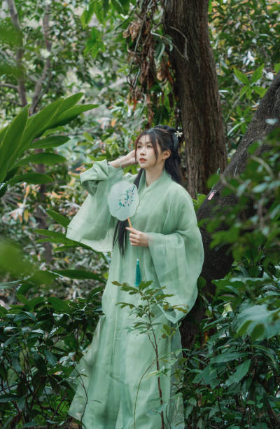 istock Graceful Hanfu Woman Leaning Against a Tree in a Lush Forest. 2202849260