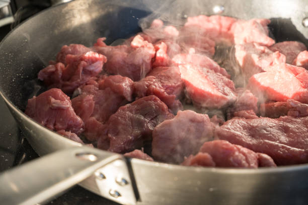 Red meat in a pan Some pieces of red meat in a smoking metal frying pan and some lateral sunlight braising pan stock pictures, royalty-free photos & images