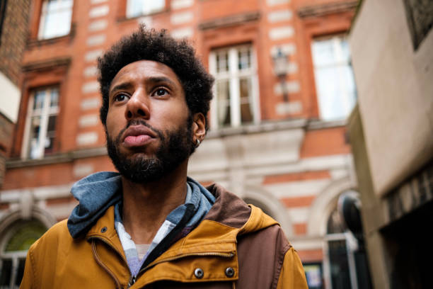 Young man looking up at building in urban setting, expressing hope and aspiration