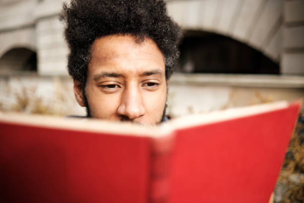 istock Young man reading a red book outdoors 2202861186