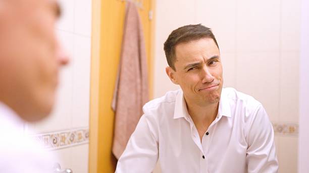 istock Businessman making funny faces in bathroom mirror 2202861791