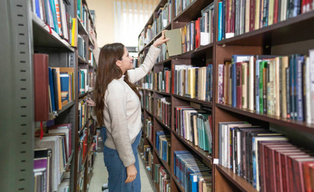 istock Young female student picking a book from library bookshelf 2202862521