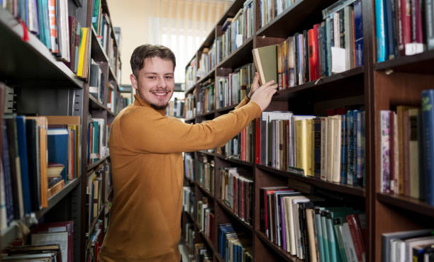 istock Young male student picking a book from library bookshelf 2202862661