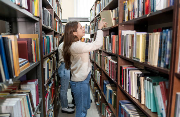 istock Young female student picking a book from library bookshelf 2202862900
