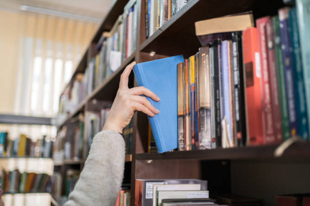istock Woman's hand picking a book from a library bookshelf 2202863107
