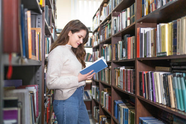 istock Young woman reading a book at library 2202863193