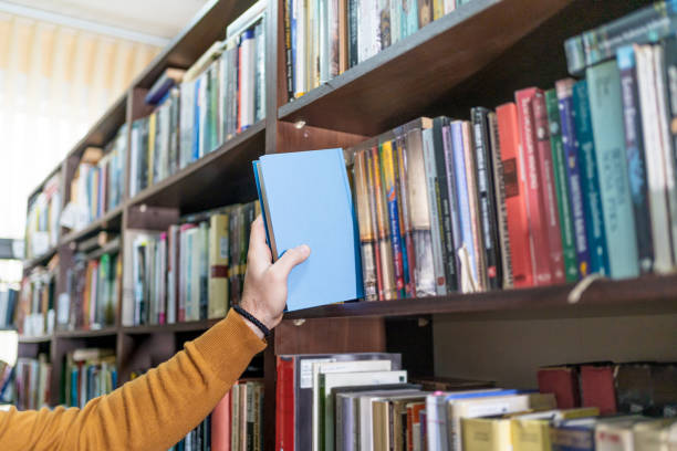 istock Man's hand picking a book from a library bookshelf 2202863311