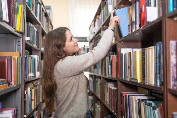 istock Young female student picking a book from library bookshelf 2202863357