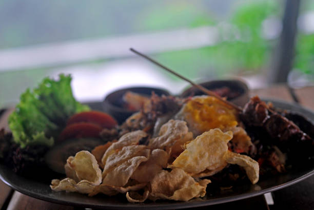 picture of delicious fried rice, with lettuce, fried egg, sambal, satay, with crackers and tomatoes. its full of taste and rich of flavor. eating it while enjoy the open space of green scenery