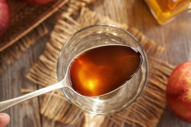Apple cider vinegar on a metal spoon above a glass of water