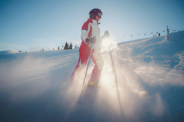 Four silhouettes of skiers in full gear moving down a snowy slope against the background of a mountain landscape at dusk, shining with headlamps