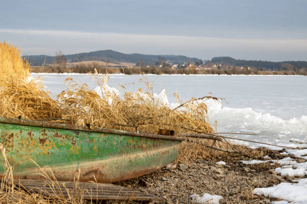 Pond (dam) Lipno, when its frozen and its too small for the ice, which is on the coast breaking. Boat on the coast. Mountains in the background. Horni Plana, Czech repbulic.