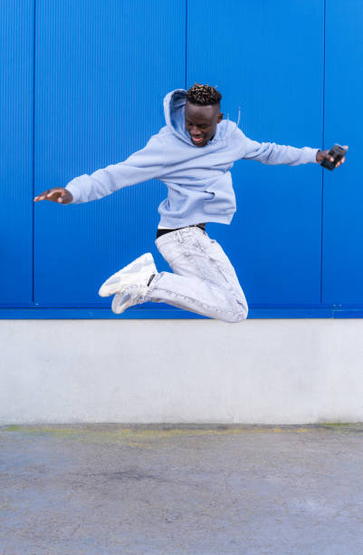 Mature Asian smiling man in casual clothes jumping on background of bright orange wall.