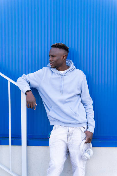 istock Young man holding headphones posing against a blue wall 2202877315