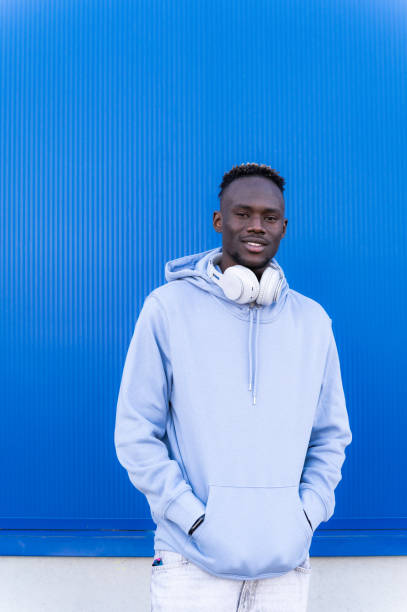istock Young man with headphones standing against a blue wall 2202877473