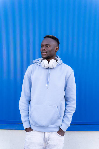 istock Young man wearing headphones looking away while standing against blue wall 2202877479