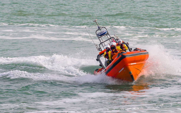 A lifeboat with an orange cover is securely placed on the upper deck of a commercial ship. The vessel showcases a blue and white design, and the weather is clear and sunny.