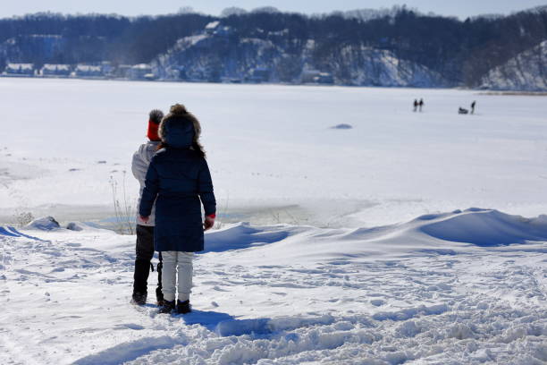 Irondequoit, NY, USA - February 22nd 2025 - Two girls watching ice fishermen pull their sled across the ice