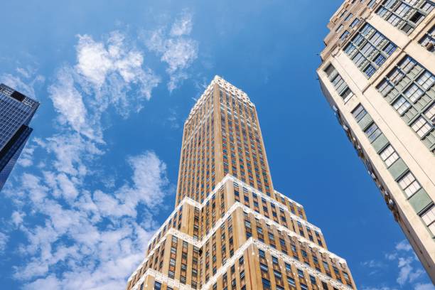 istock Low-angle view of tall brick skyscraper with decorative facade against blue sky with white clouds. New York. USA. 2202883967