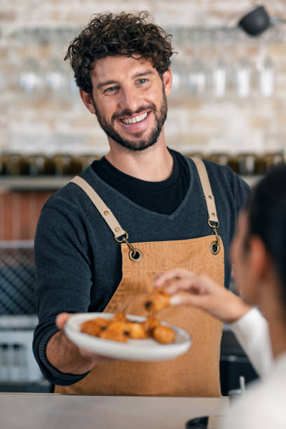 istock Handsome waiter talking with a client while serving chocolate croissants in the pastry shop. 2202889549