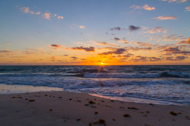 Golden sunrise paints the sky with vibrant colors as gentle waves roll onto a serene sandy beach