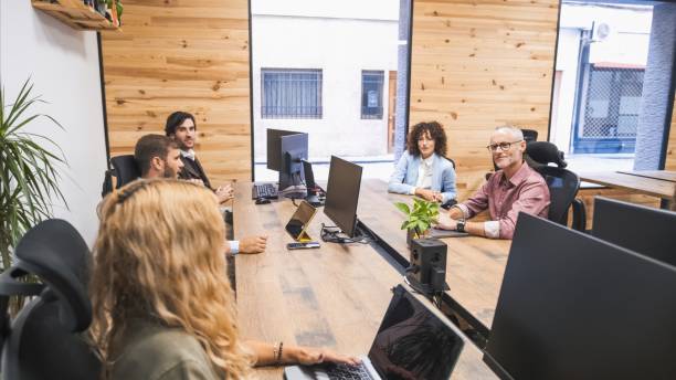 istock Mature businessman looking at colleagues while sitting at computer desks in office 2202893500