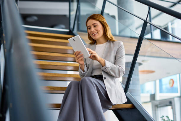 istock Businesswoman using digital tablet sitting on stairs in modern office 2202893599