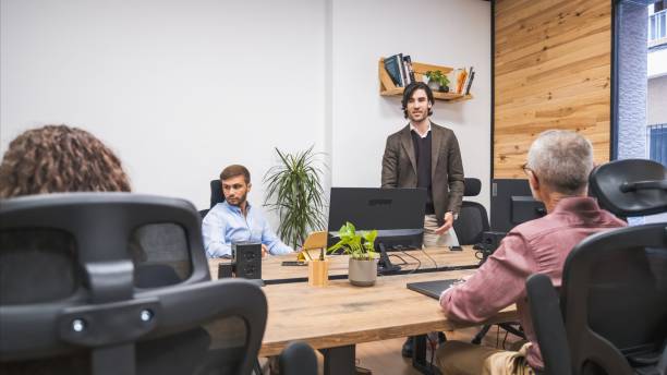 istock Confident businessman talking to team sitting at computer desks in creative office 2202893615