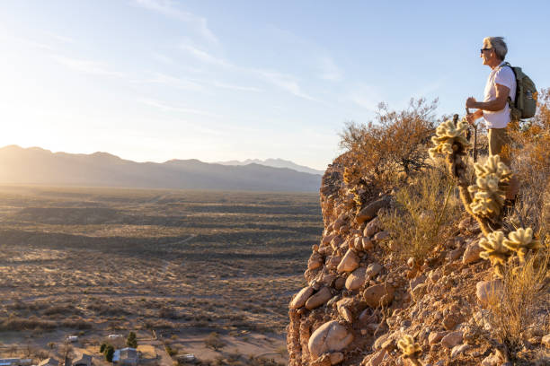 Mature man stands on edge of cliff at sunset and looks towards mountains, Tonto Basin, AZ