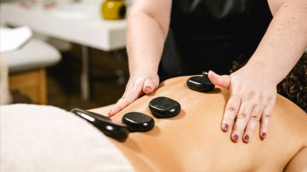 istock Masseuse placing hot stones on client's back during spa treatment 2202897959