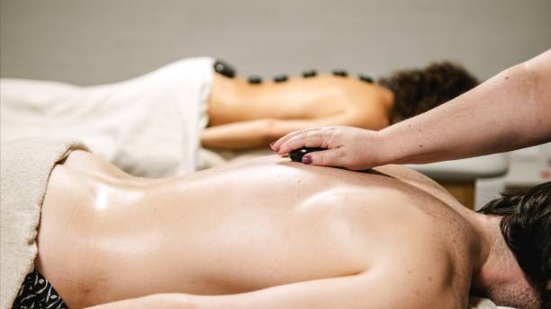 istock Masseuse placing hot stones on client's back during couple massage 2202898903