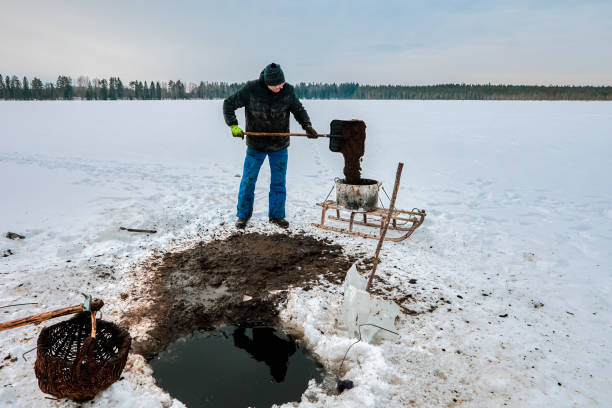 istock Ice hole sapropel extraction involves farmer using basket to collect goo, shoveling it to tank, and moving sludge via sled for organic agriculture. 2202904380
