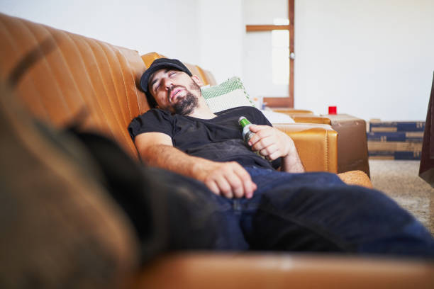 istock Man sleeping on couch after partying with beer bottle in hand 2202906704