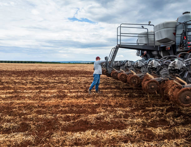 A large, advanced planting machine is seen working on a vast farmland.. The machinery's multiple components and precision technology highlight the efficiency and scale of modern farming practices. The expansive field and clear sky emphasize the rural setting.