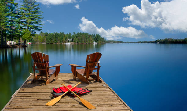 istock Adirondack chairs on a dock with paddles, life jackets nearby. 2202913298