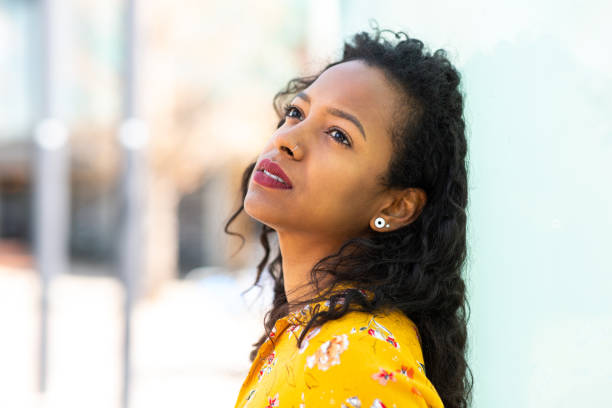 istock Serious young african woman leaning against wall looking up 2202920704