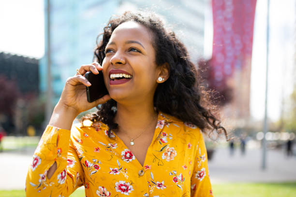 istock Smiling young african woman talking on cell phone standing outside 2202920911