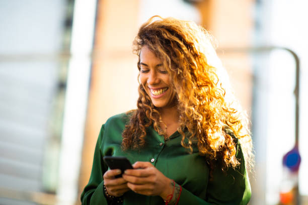 istock Cheerful young latin woman text messaging on cellphone outside 2202921491